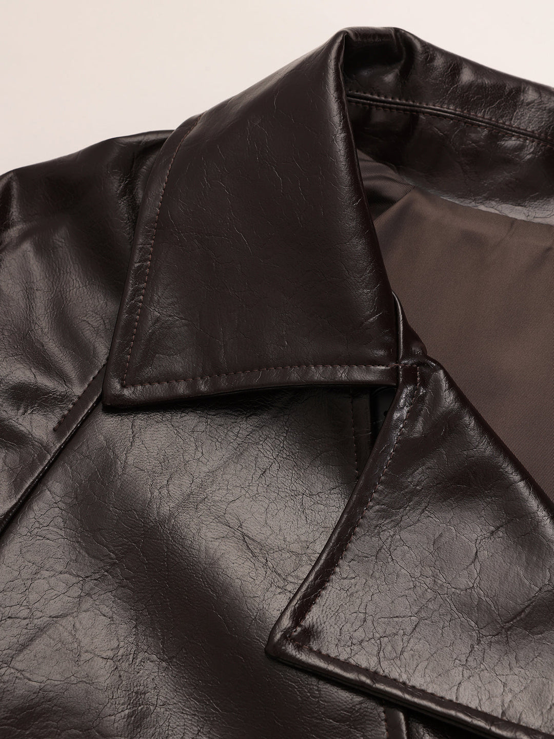 Detail of the wide collar and open lapel of the dark brown vegan leather trench