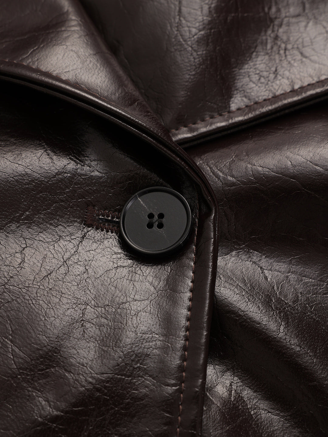 Close-up of the black four-hole button and topstitched lapel on the brown leather coat