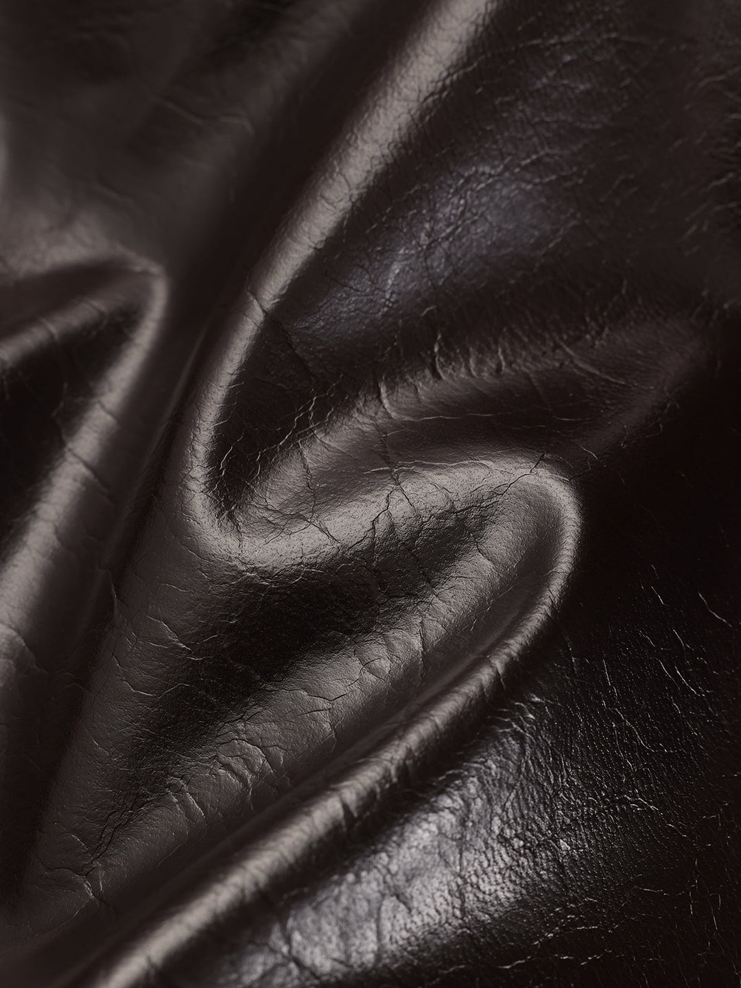 Macro of the glossy crinkled brown faux leather fabric in soft folds