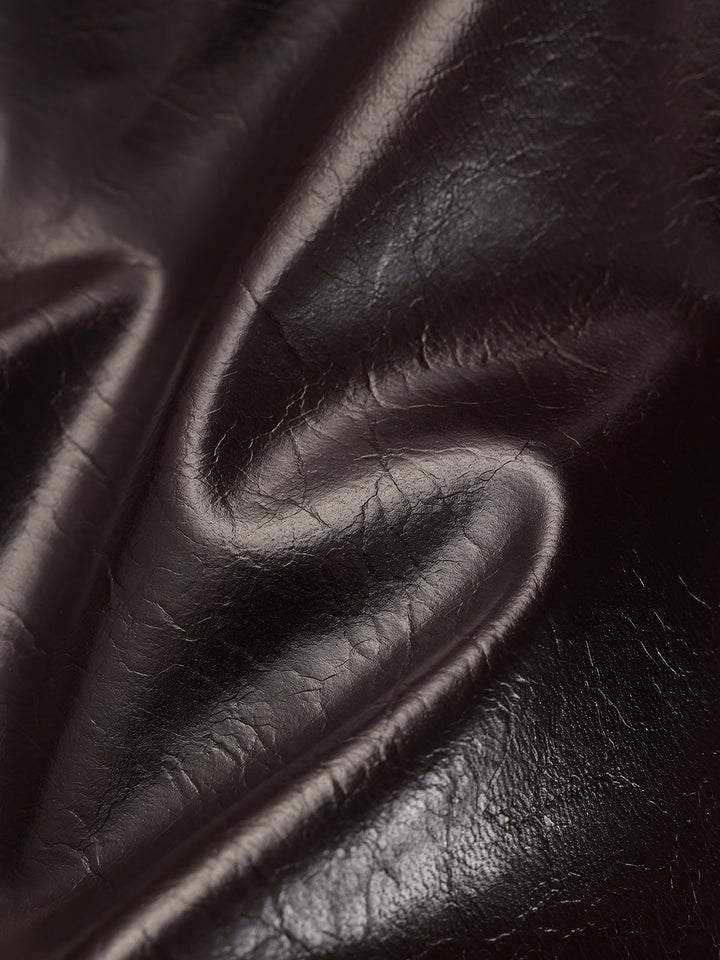 Macro of the glossy crinkled brown faux leather fabric in soft folds