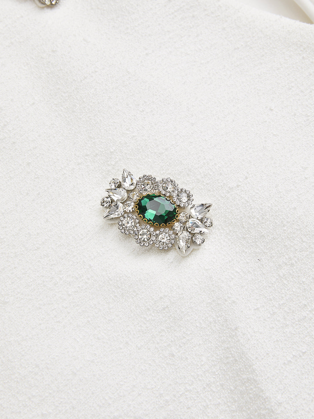 Close-up of the emerald and clear rhinestone jewel appliqué on the white top