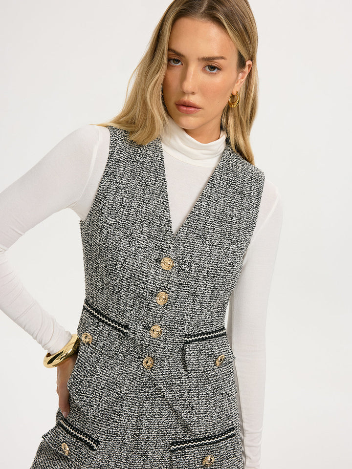 Grey tweed V-neck vest with gold buttons layered over white turtleneck