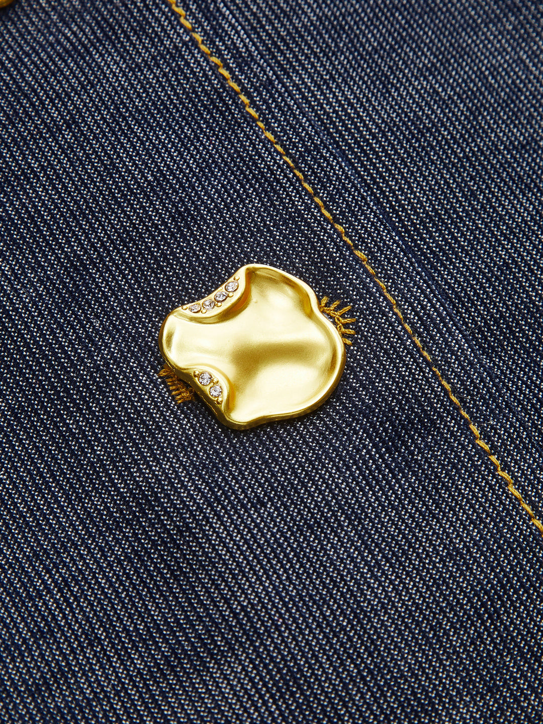 Macro of gold crystal-set metal button on navy denim sleeveless vest