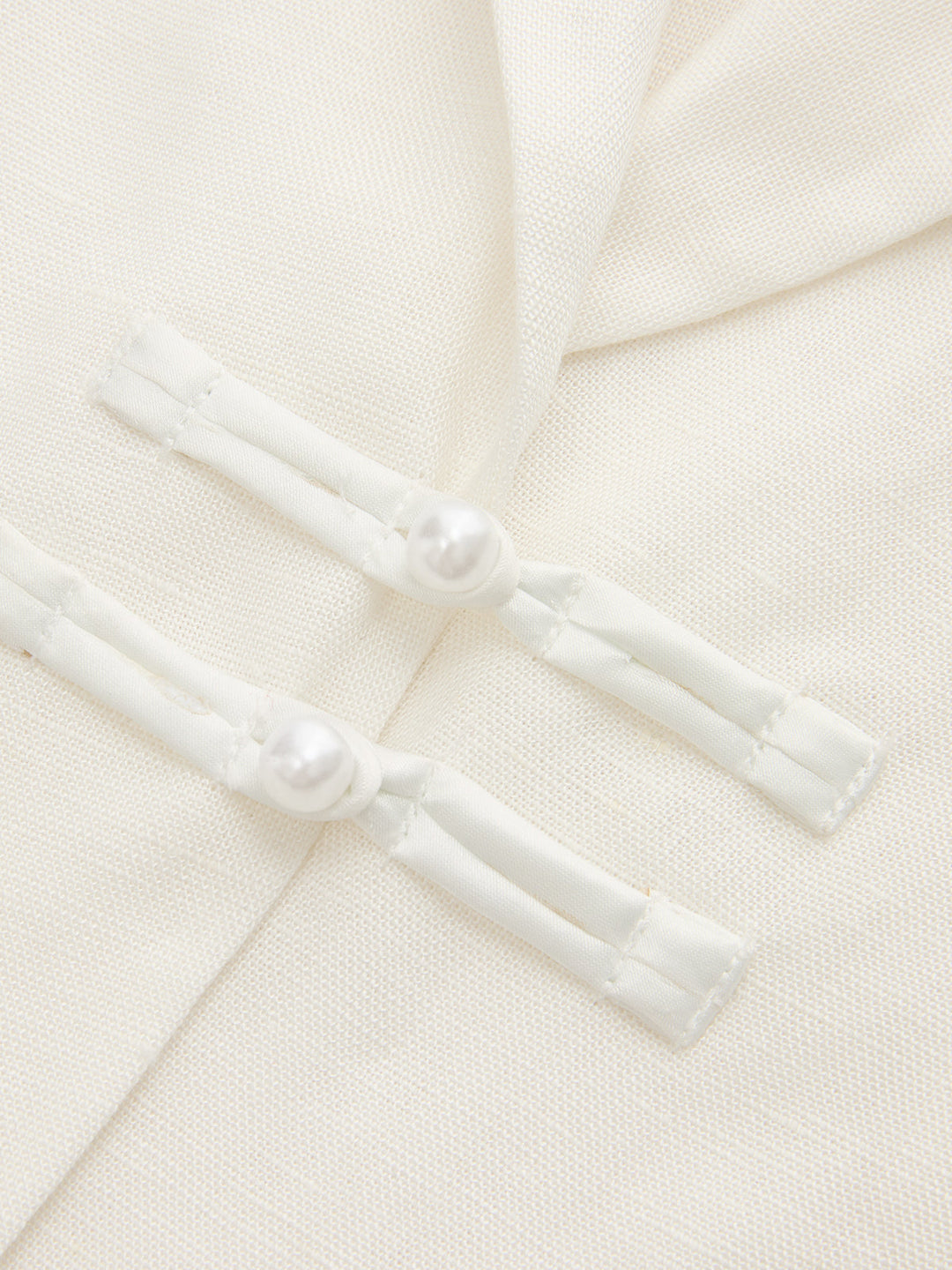 Close-up of the pearl frog button closures on the ivory linen blend blazer vest