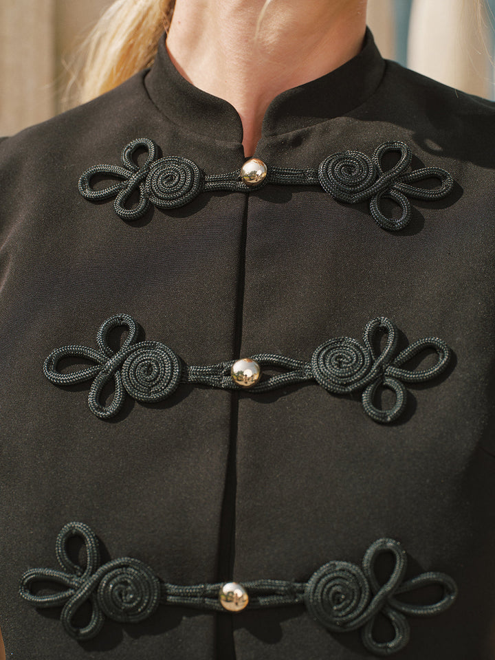 Close-up of black soutache frog knot fastenings and gold ball buttons on the vest
