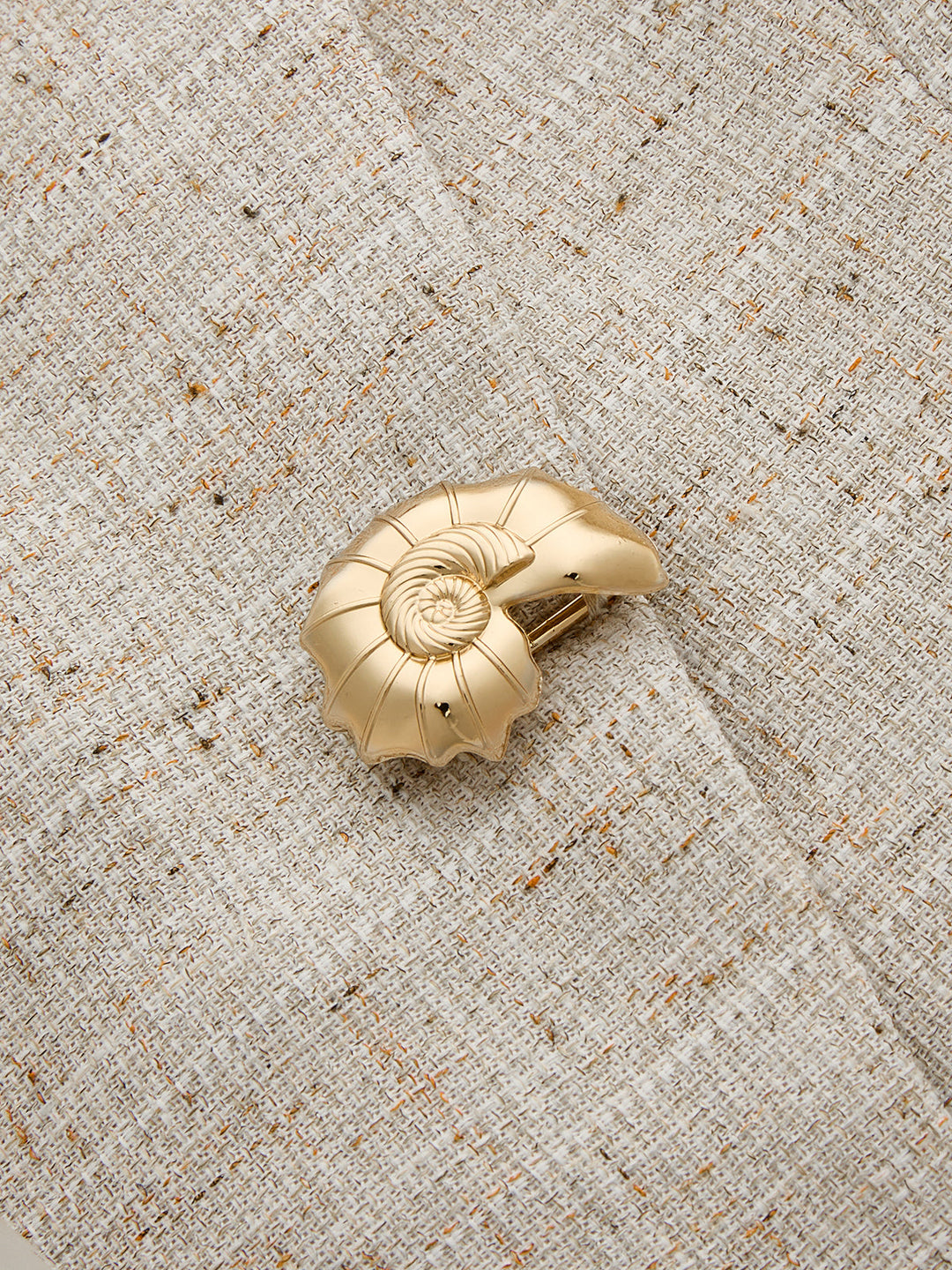 Close-up of brushed gold seashell button on the beige slub tweed vest