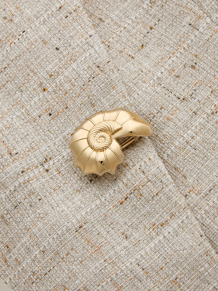 Close-up of brushed gold seashell button on the beige slub tweed vest