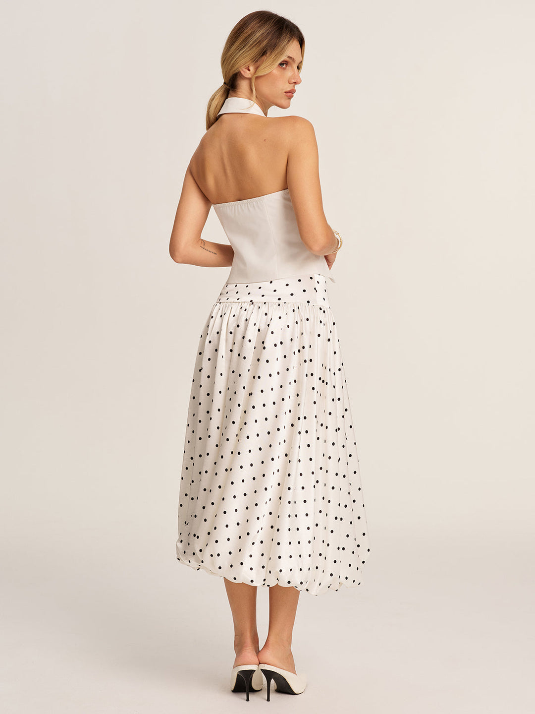 Back view of the open-back halter blazer vest showing bare back and neck strap, styled with heels