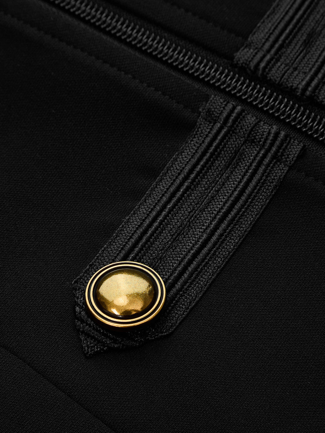 Detail of domed gold button, braided trim and silver zipper on the black military vest