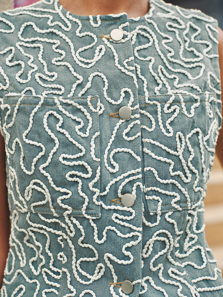 Macro of the white swirl cord embroidery stitched onto the light blue denim