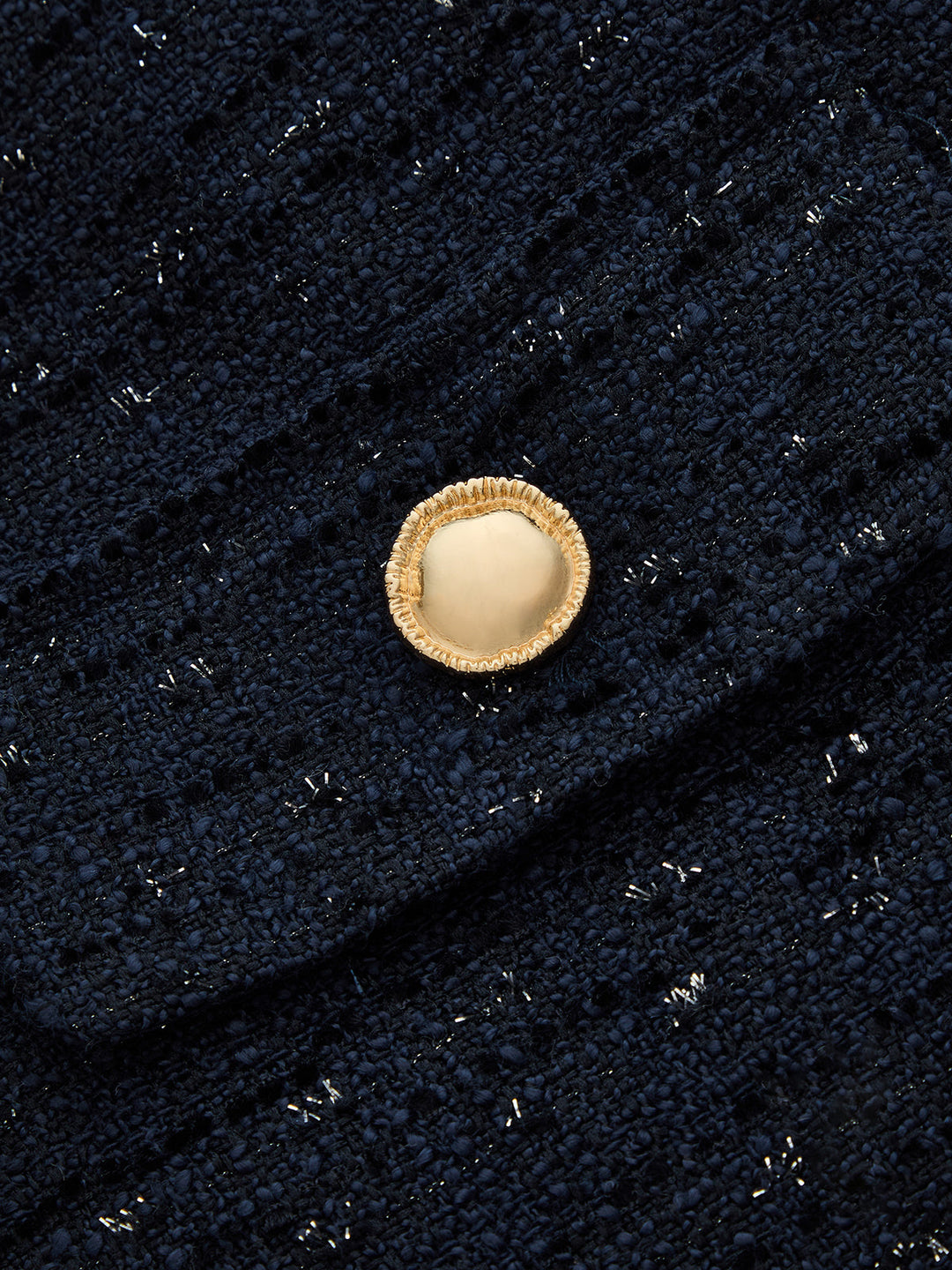 Detail of a gold dome button on navy tweed shot through with metallic silver threads
