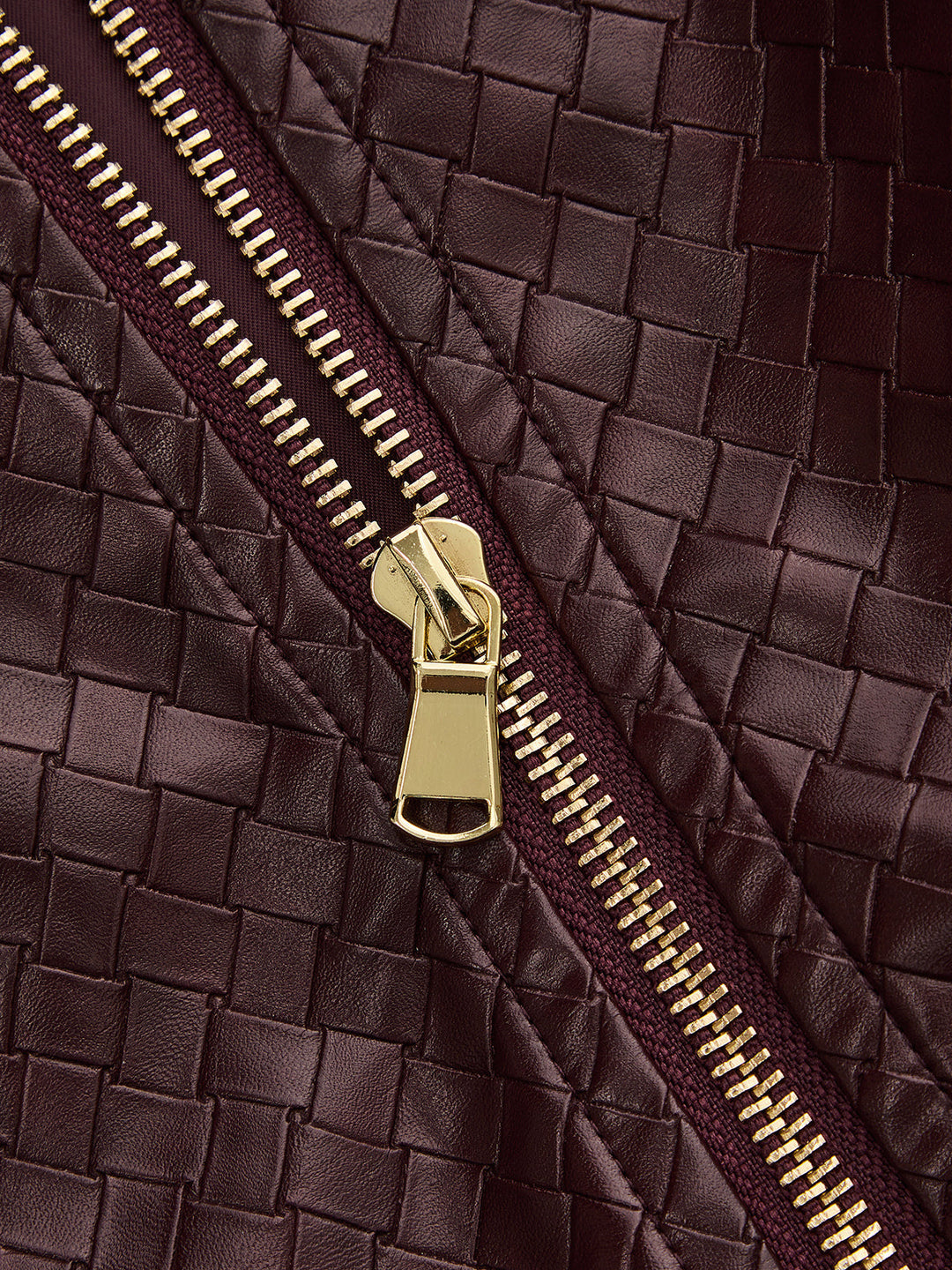 Close-up of gold zip pull against the woven burgundy faux leather