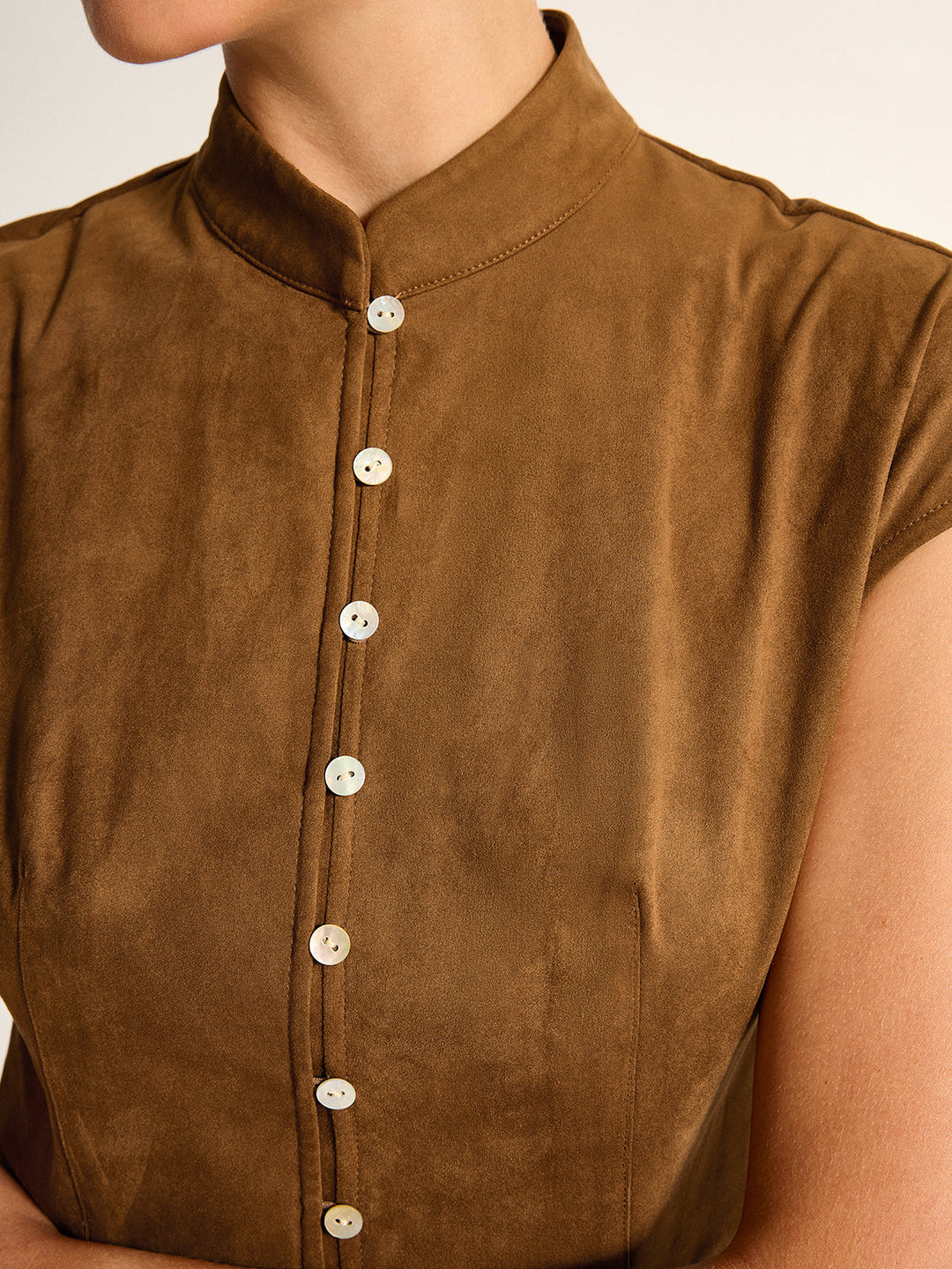 Close-up of mandarin collar and row of pearl buttons on brown suede-effect top