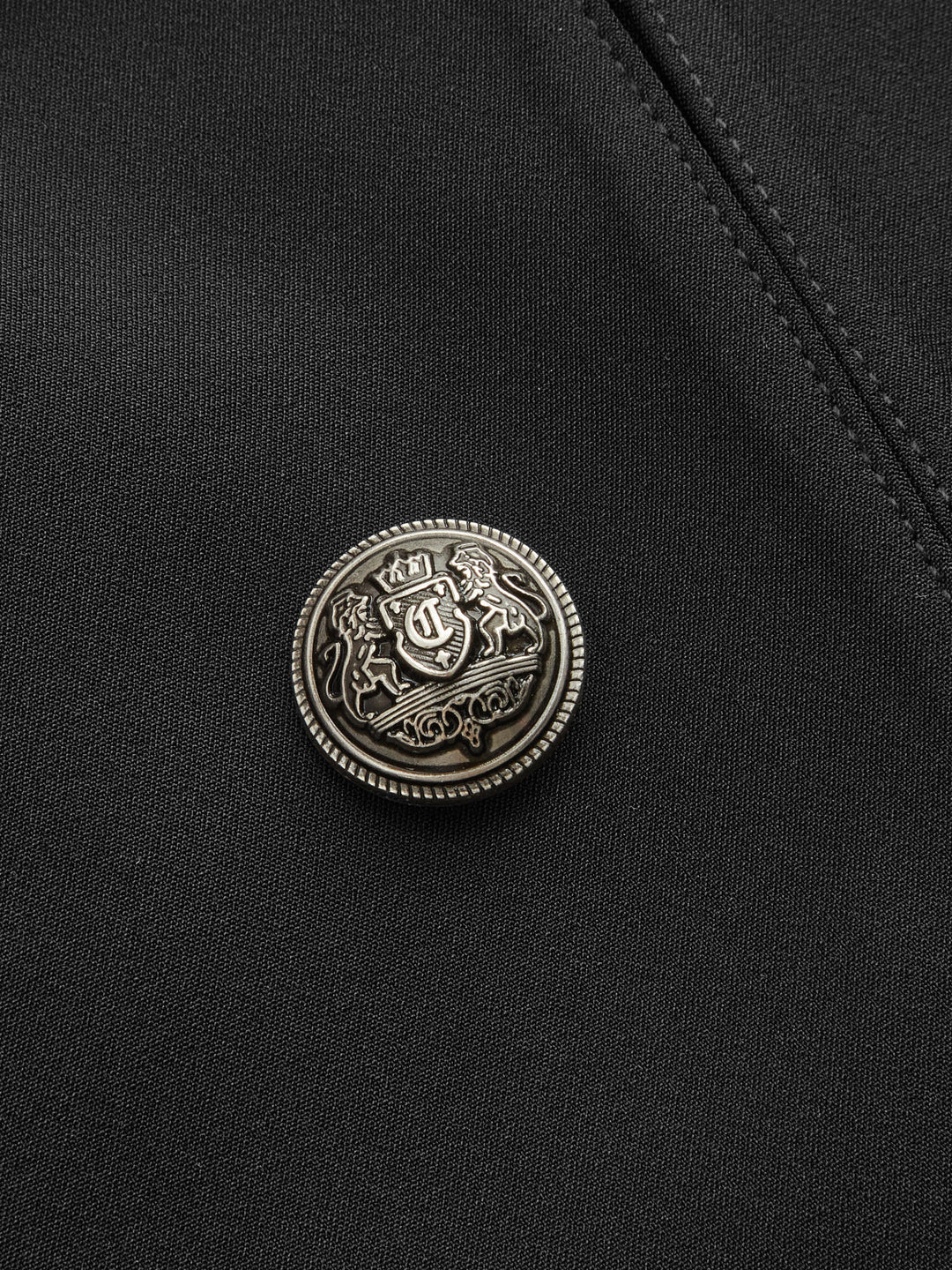 Close-up of the antique silver crest button on black jacket fabric