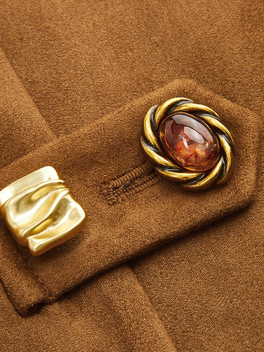 Close-up of the ornate gold and amber frog button closure on camel suede fabric