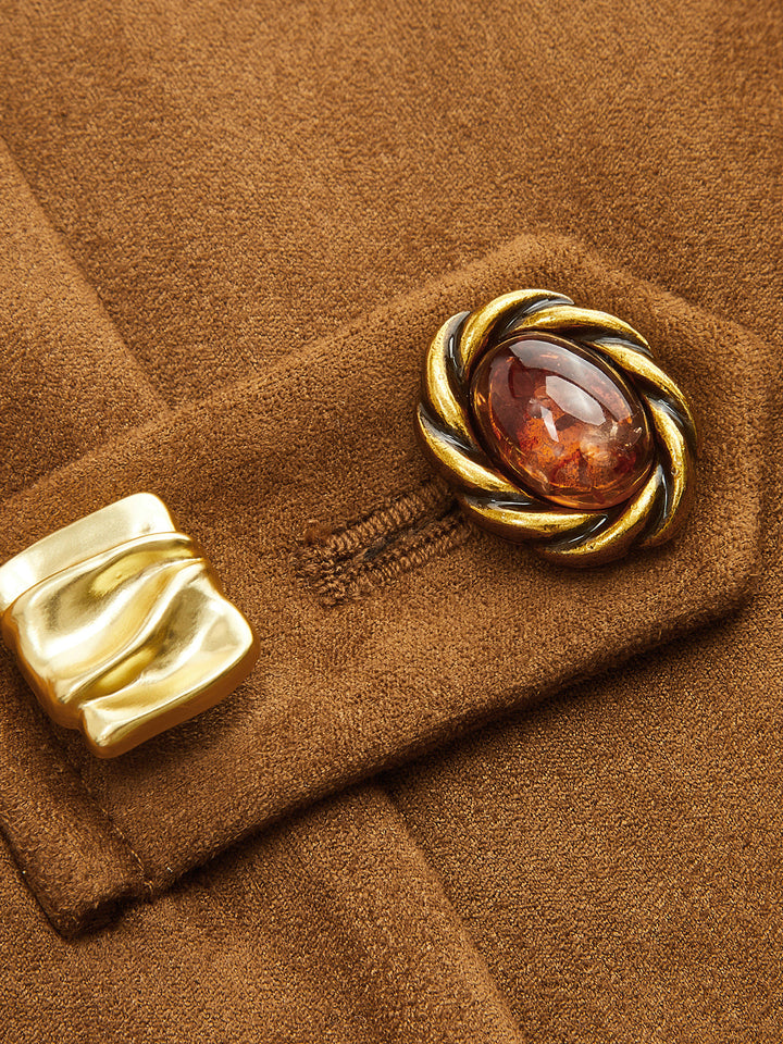 Close-up of the ornate gold and amber frog button closure on camel suede fabric