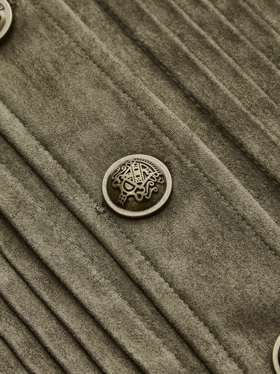 Detail of the ornate antique gold crest button and vertical pintucks on the green jacket