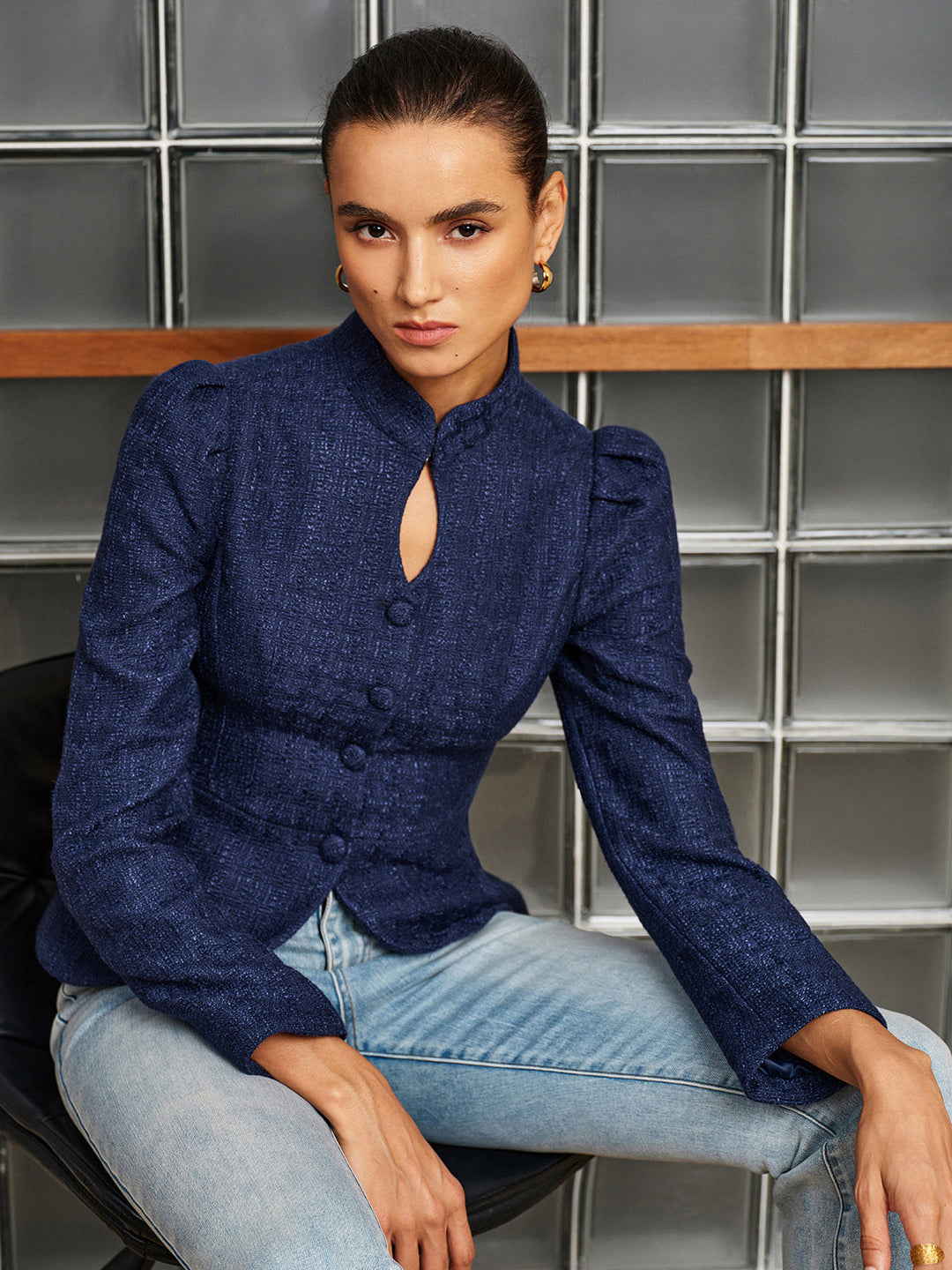 Model seated in a navy tweed peplum jacket with stand collar, worn with light wash jeans