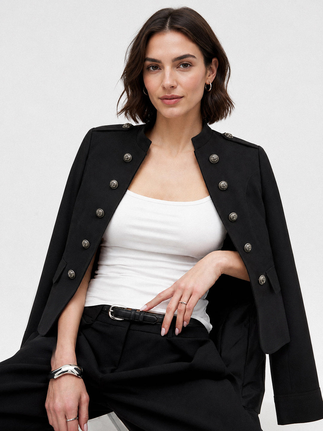 Model wearing black double-breasted military jacket open over white tank and black trousers