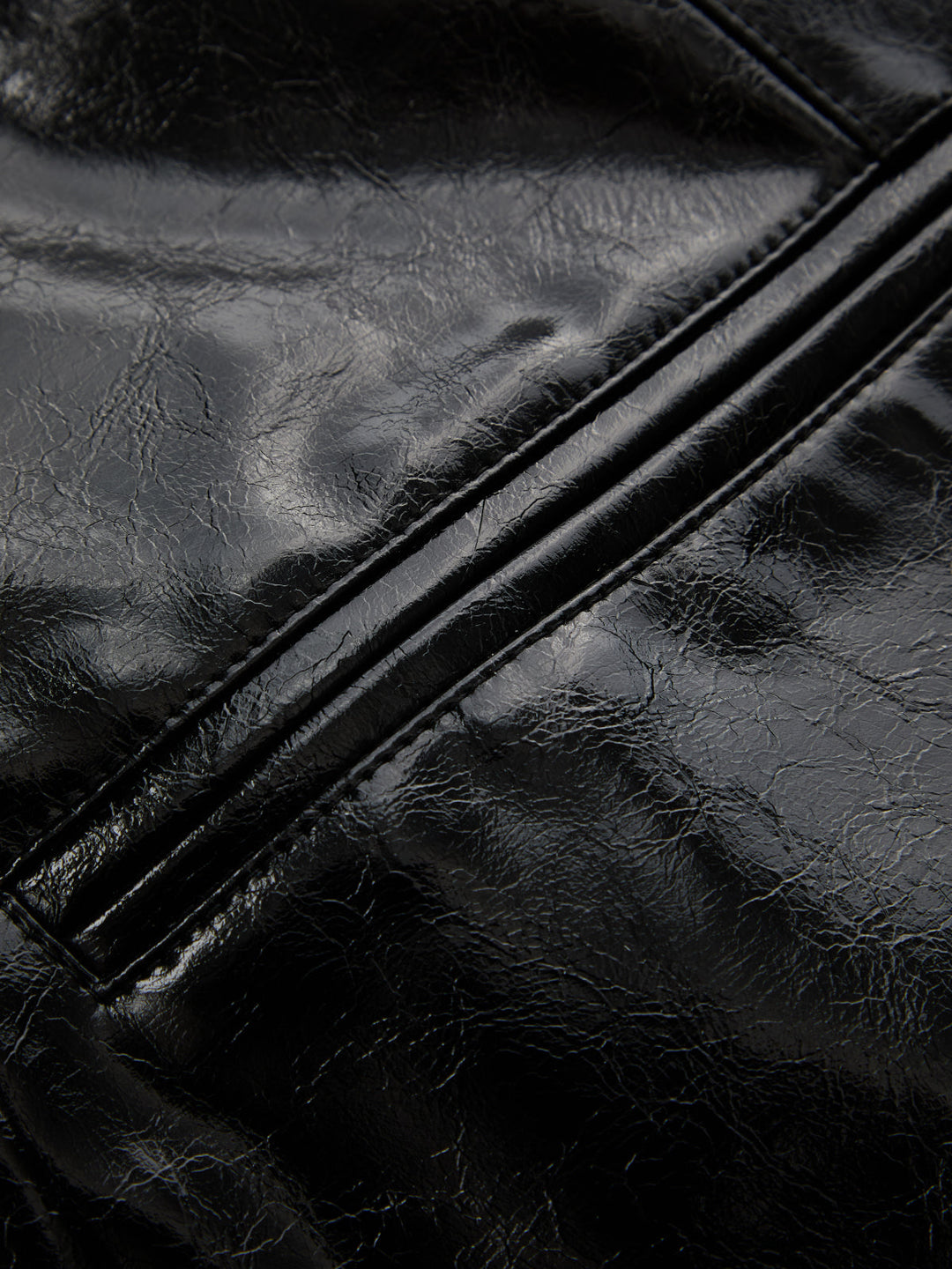 Detail of the welt pocket and crinkled high shine black leather look fabric