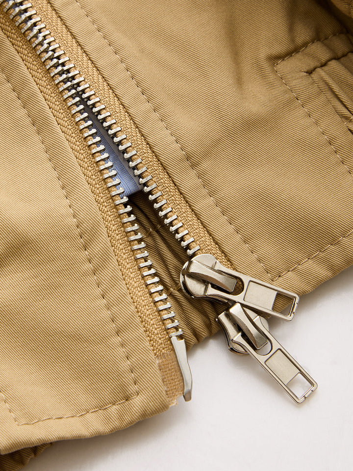 Close-up of the gold double zipper and topstitched pocket on the tan bomber jacket