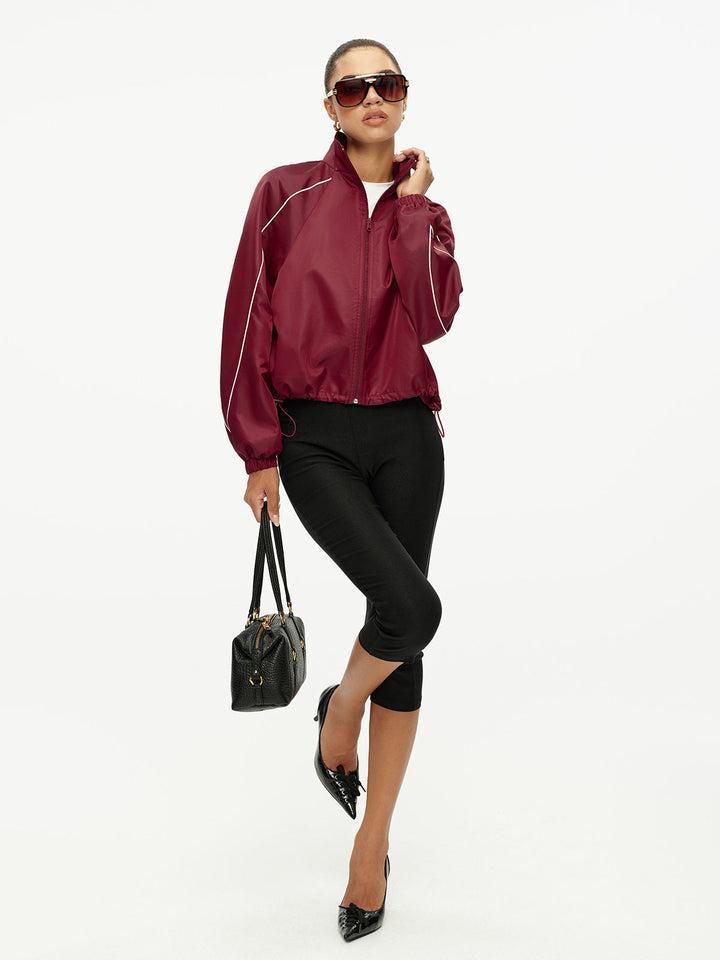 Full-length walking shot of the burgundy retro track jacket with black handbag
