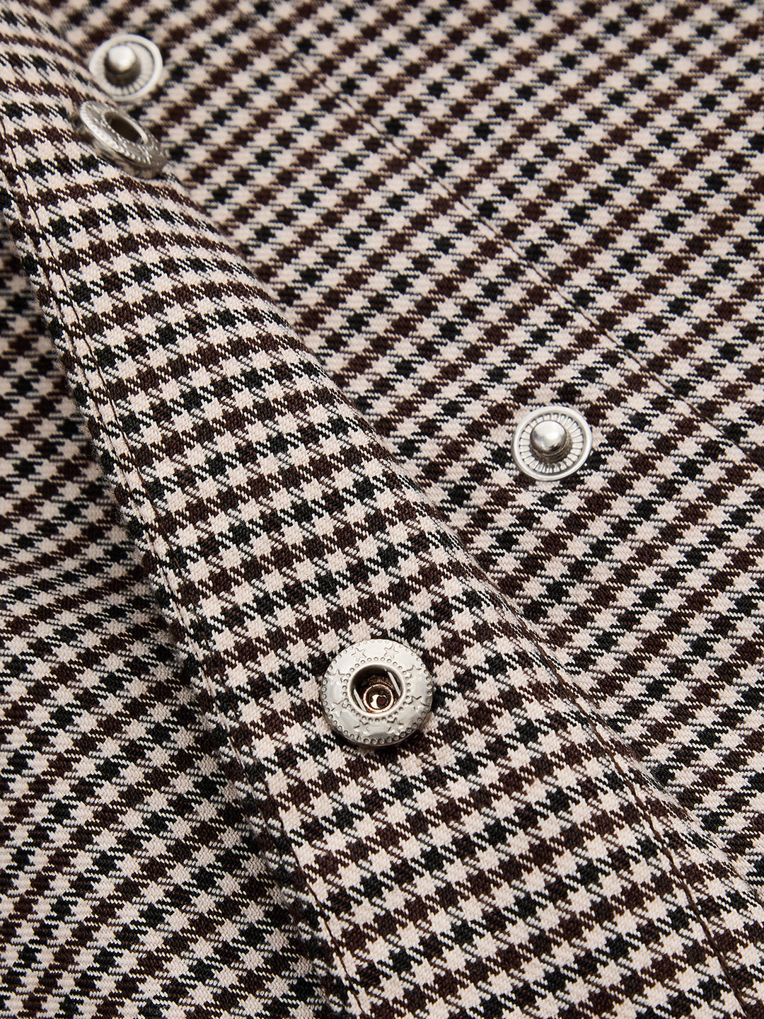 Close-up of silver dome buttons on the cuff of a houndstooth tie collar jacket