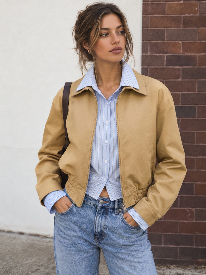 Khaki bomber jacket with built-in striped shirt collar, worn with jeans against a brick wall