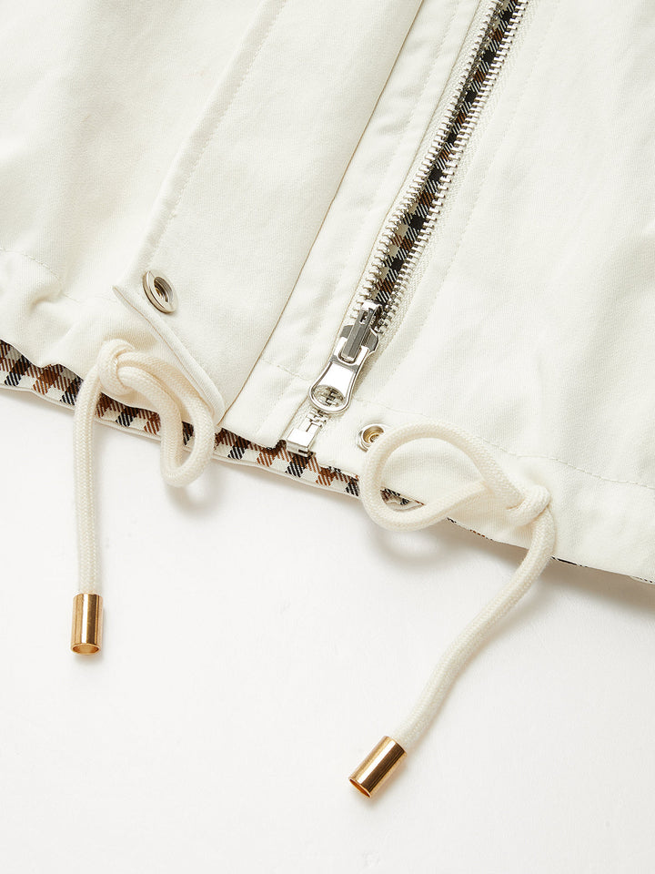 Close-up of gold-tipped drawstring cords and zip on the cream jacket hem