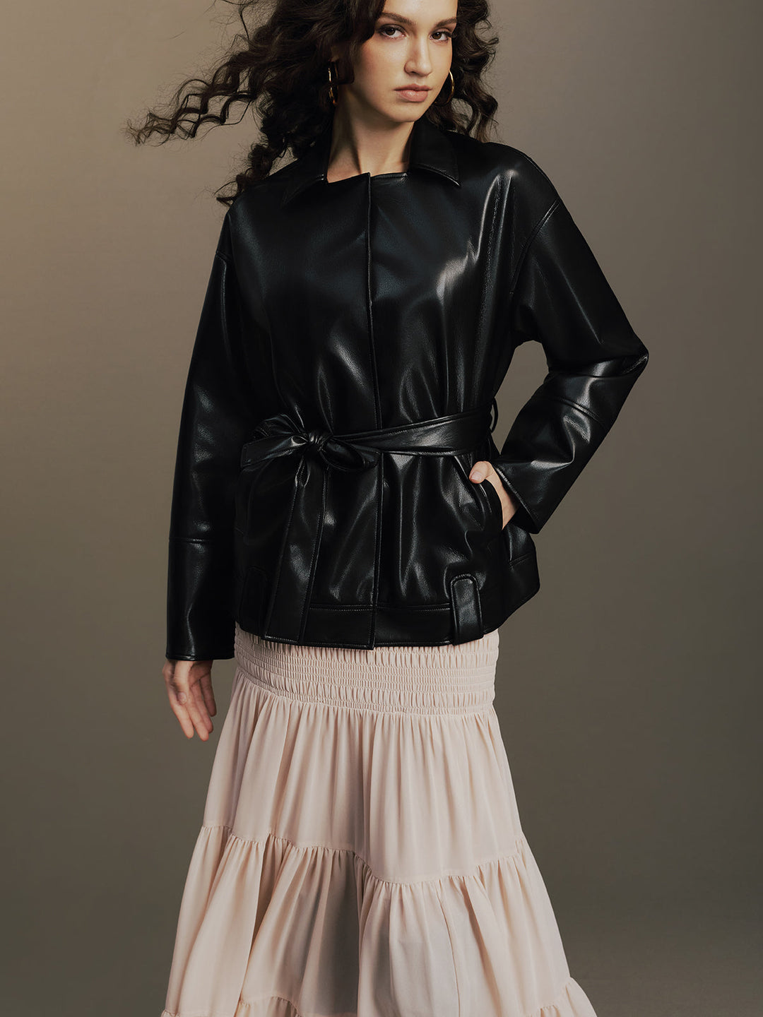 Three-quarter view showing the knotted belt and side pockets of the leather jacket