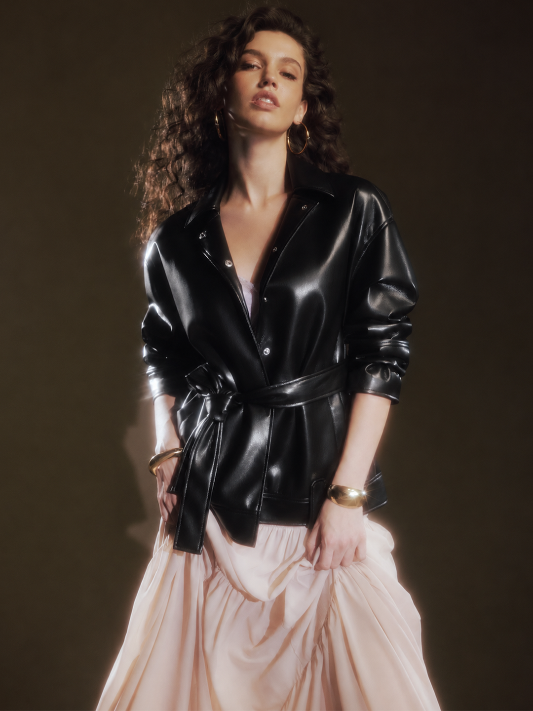 Editorial shot of the glossy black leather jacket styled over a blush tiered maxi skirt