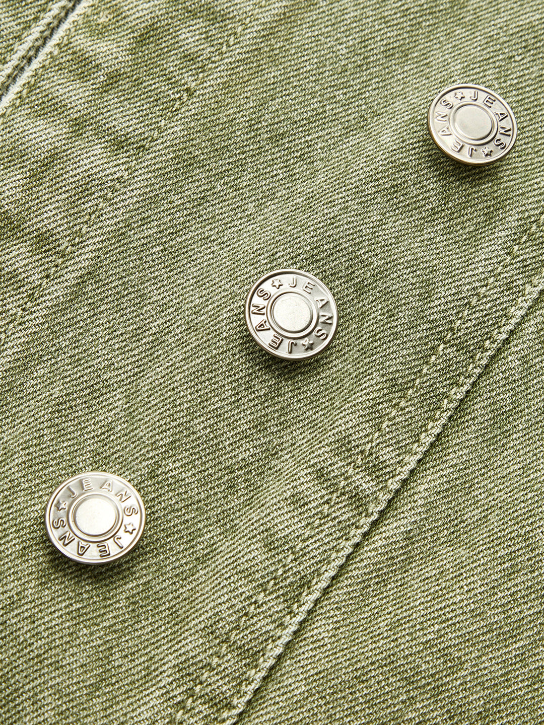 Close-up of the engraved silver buttons on the green denim placket