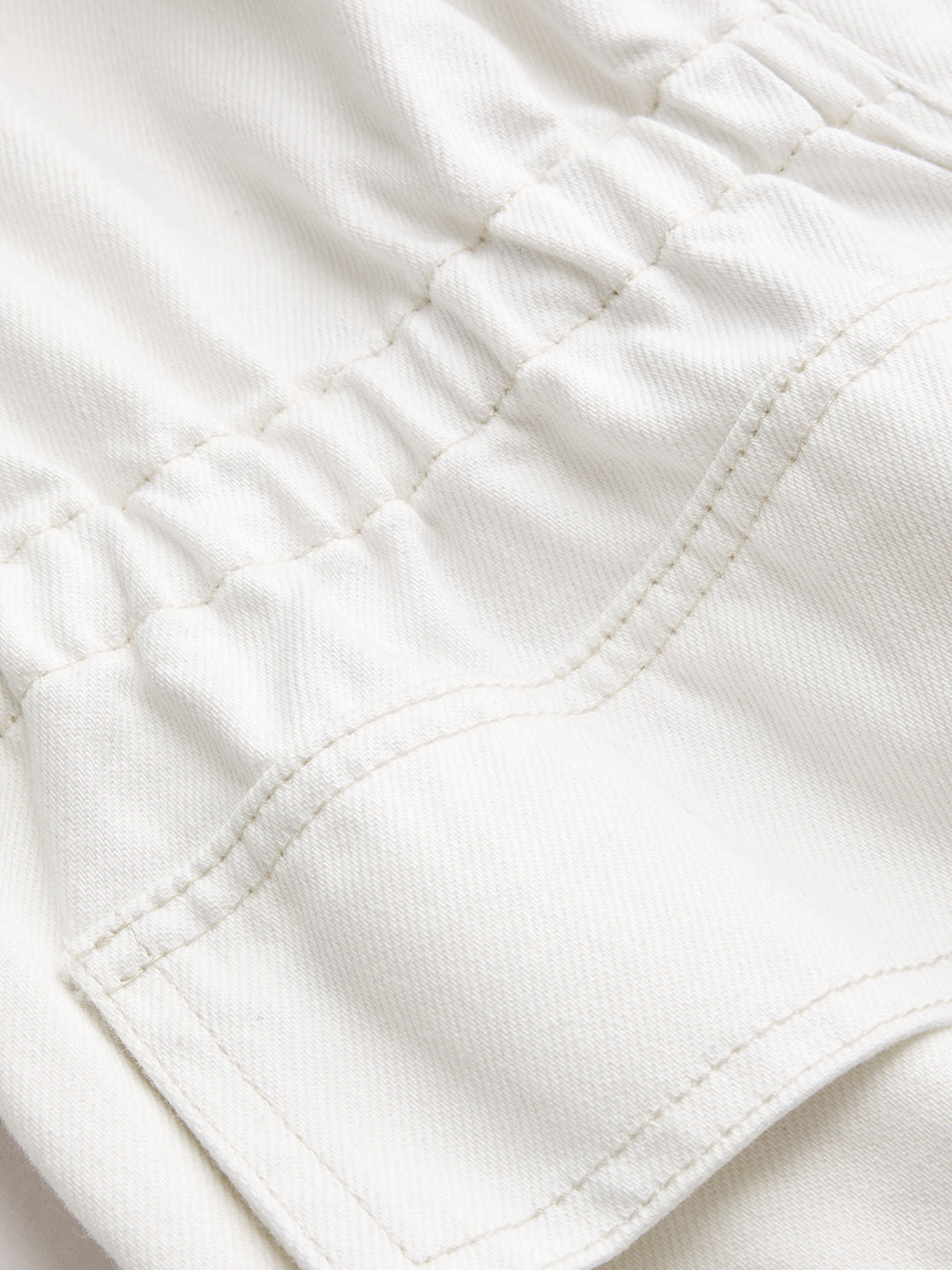 Close-up of elastic waist shirring and flap pocket topstitching on white denim jacket