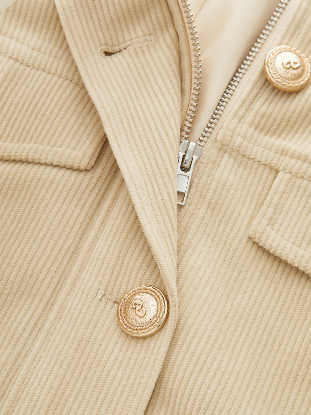 Close-up of the open collar, zip and ornate gold button on the khaki corduroy jacket