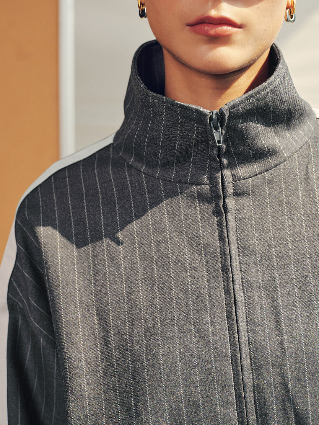 Close-up of the high funnel collar and zip front on the grey pinstripe track jacket