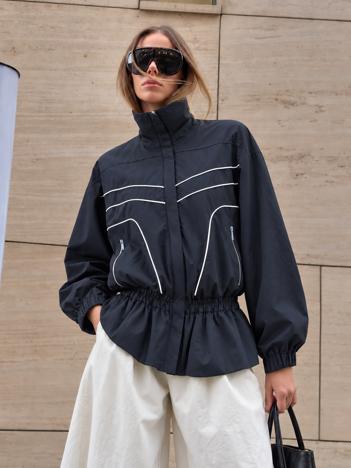 Navy windbreaker jacket with white piping worn with cream wide leg trousers
