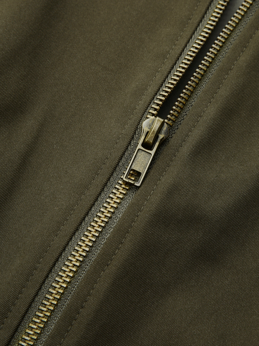 Detail of the antique gold front zip on olive bomber jacket fabric