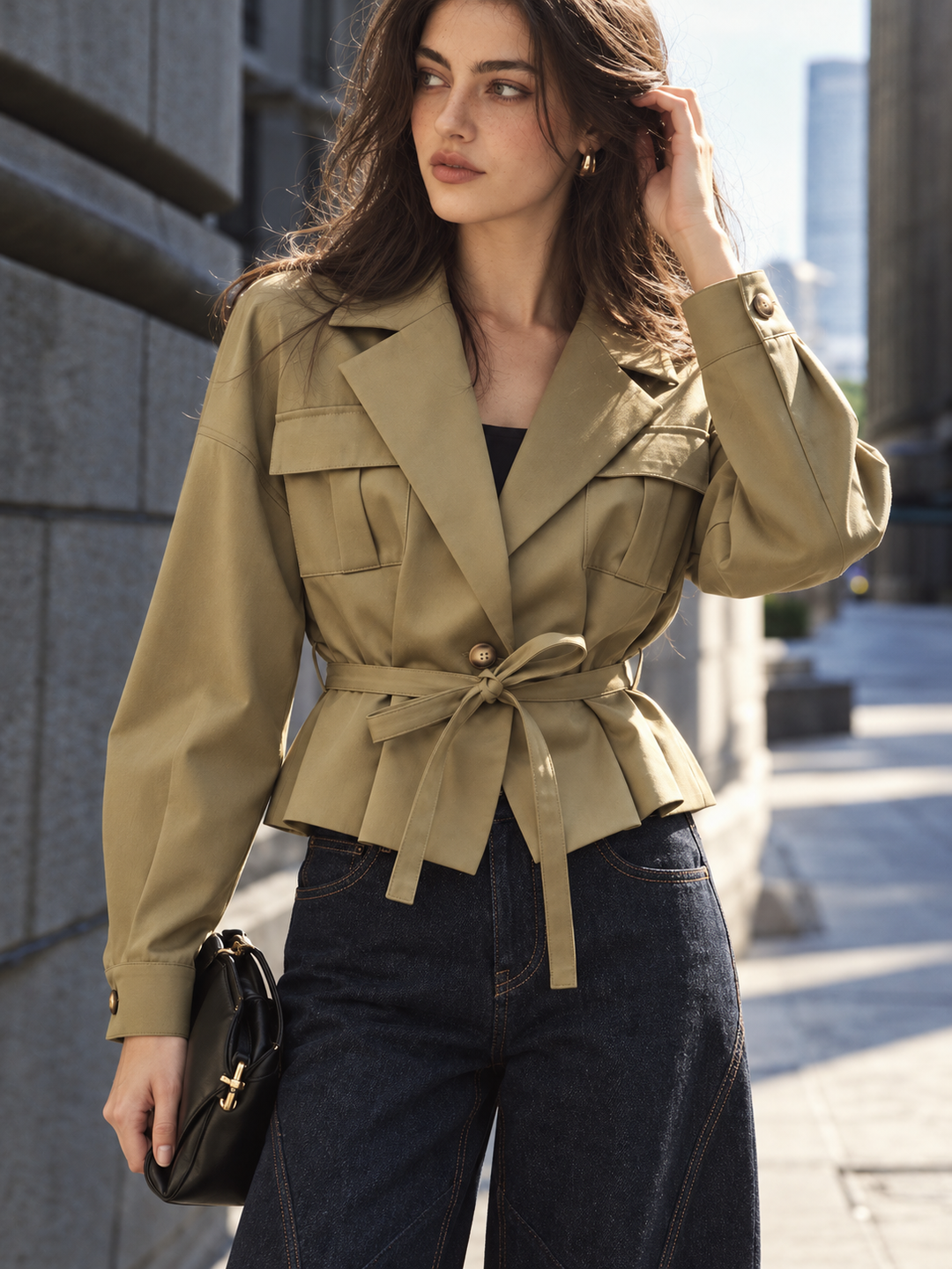 Model in khaki belted utility jacket with notch lapels, dark jeans and black bag