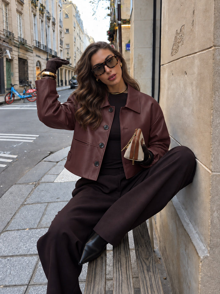Model in Paris wearing burgundy relaxed faux leather jacket with brown wide-leg trousers