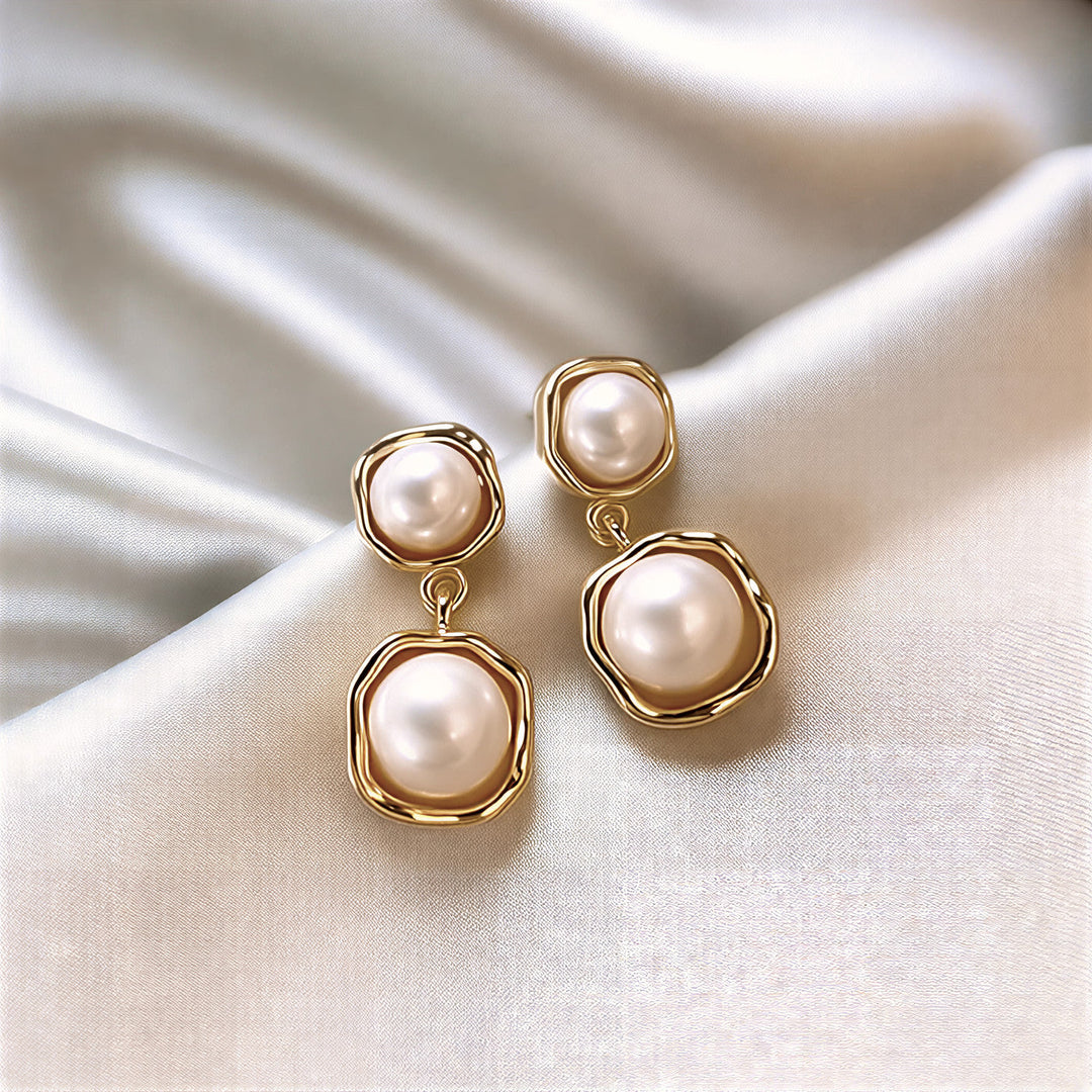 Gold-tone framed pearl drop earrings laid flat on a plain background