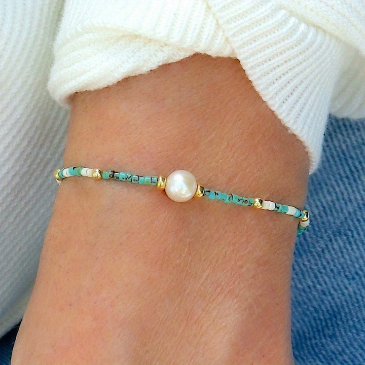 Turquoise pearl bracelet coiled beside its jewellery packaging