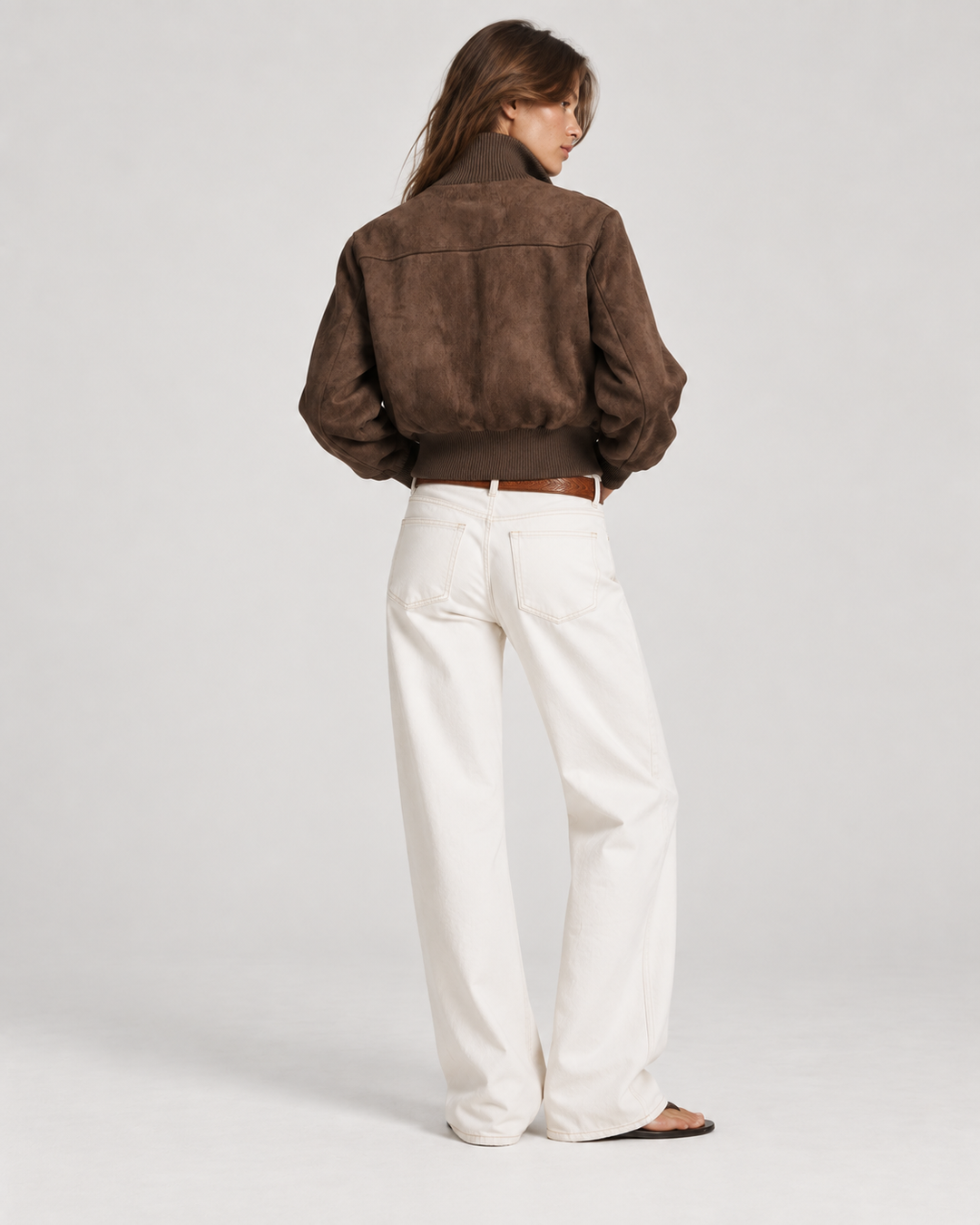 Back view of dark brown suede bomber jacket for women, cropped fit over white denim