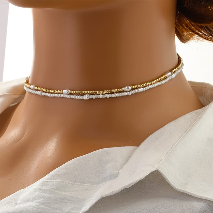 Layered gold and pearl necklace set laid flat on a white background