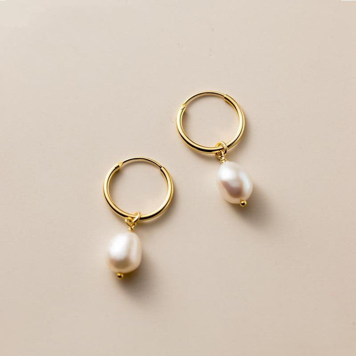 Pearl hoop earrings laid flat next to soft draped fabric