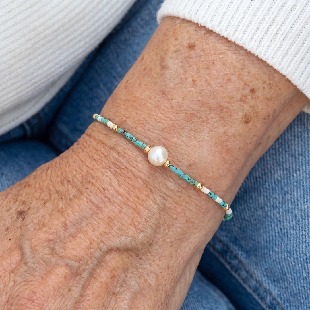 Turquoise and pearl beaded bracelet laid flat on a plain background